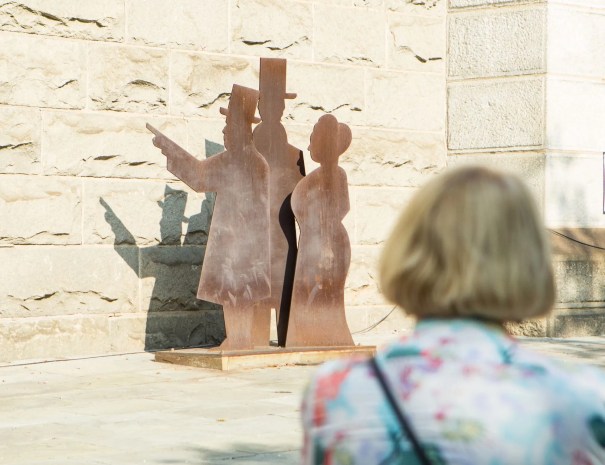 Visitor looking at silhouette sculpture A person views a metal silhouette sculpture of three historic figures in Victorian attire, mounted against a stone wall near the bridge.