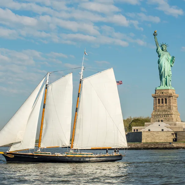 Schooner America 2.0 sailing in New York Harbor with the Statue of Liberty in the background
