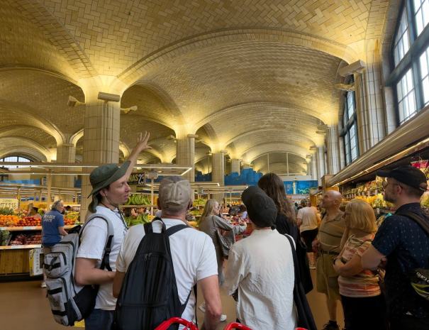 _11 — Guide gestures up at the vaulted Guastavino tile ceiling inside the Trader Joe's at Bridgemarket, under the Queensboro Bridge, as the group looks on.