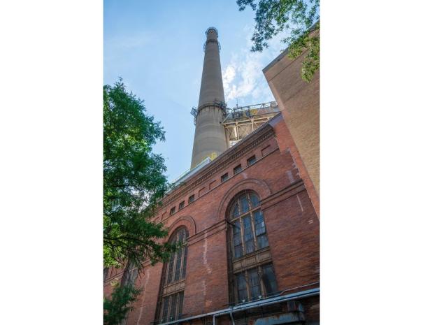 Looking up at the arched windows of a red brick powerhouse with its concrete smokestack towering overhead.