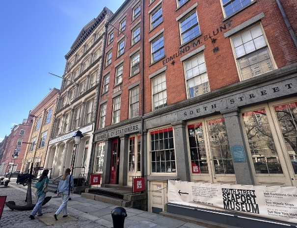 Row of 19th-century commercial brick buildings along Water Street at the South Street Seaport Museum, with pedestrians on the sidewalk