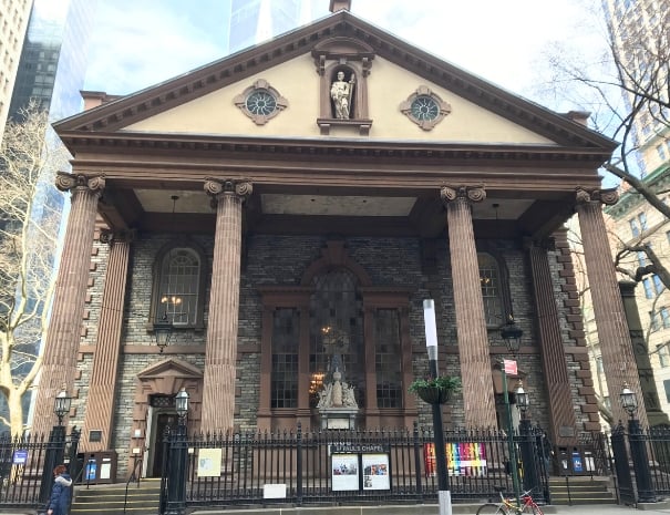 Neoclassical facade of St. Paul's Chapel in lower Manhattan, featuring Ionic columns, a triangular pediment with a saint's statue, and a stone exterior