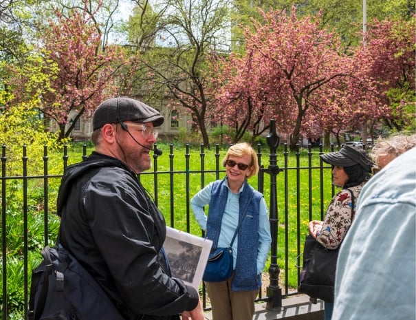 Untapped New York tour guide discussing history with guests in front of blooming pink cherry trees at a Manhattan park during a Spies of the American Revolution walking tour