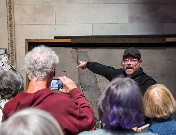 Untapped New York guide pointing to the First Inaugural Day April 30, 1789 marker inside Federal Hall National Memorial while guests photograph the historic site