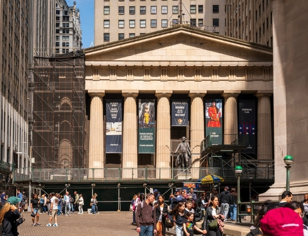 The neoclassical exterior of Federal Hall National Memorial on Wall Street in lower Manhattan, with a statue of George Washington on the steps and exhibit banners on the columns