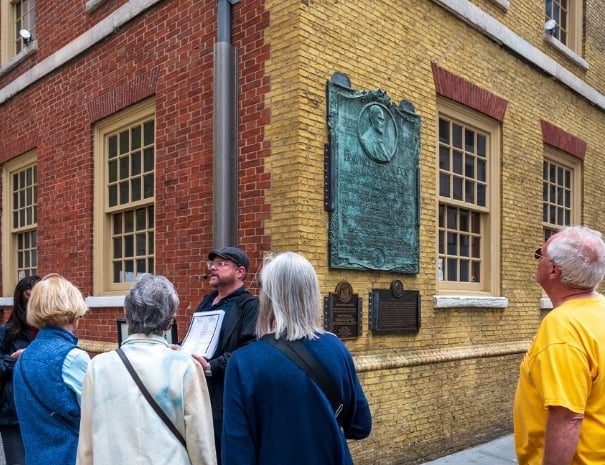 ntapped New York tour group examining a large bronze commemorative plaque on Fraunces Tavern in lower Manhattan