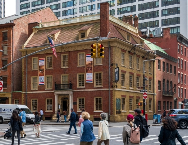 The exterior of Fraunces Tavern at the corner of Pearl and Broad Streets in lower Manhattan, a Georgian-style landmark dating to 1719 with an American flag displayed on the facade