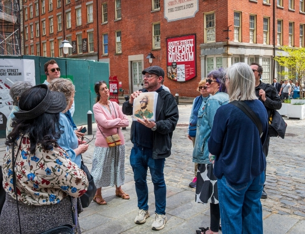 Untapped New York tour guide showing guests a historical portrait in front of the South Street Seaport Museum in lower Manhattan during the Spies of the American Revolution walking tour