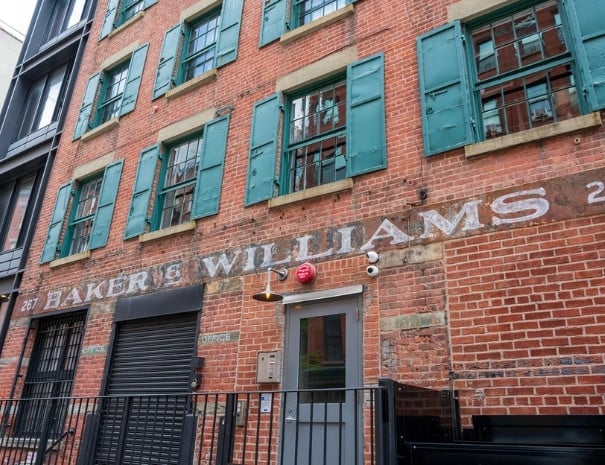 Close-up of the historic Baker & Williams warehouse building at 267 Water Street in lower Manhattan, featuring faded painted lettering on a red brick facade with green shuttered windows