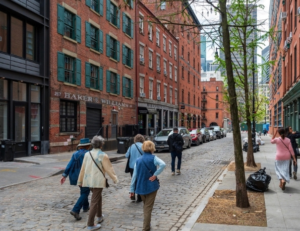 Tour guests walking along a cobblestone street past the historic Baker & Williams warehouse at 267 Water Street in the South Street Seaport neighborhood of lower Manhattan