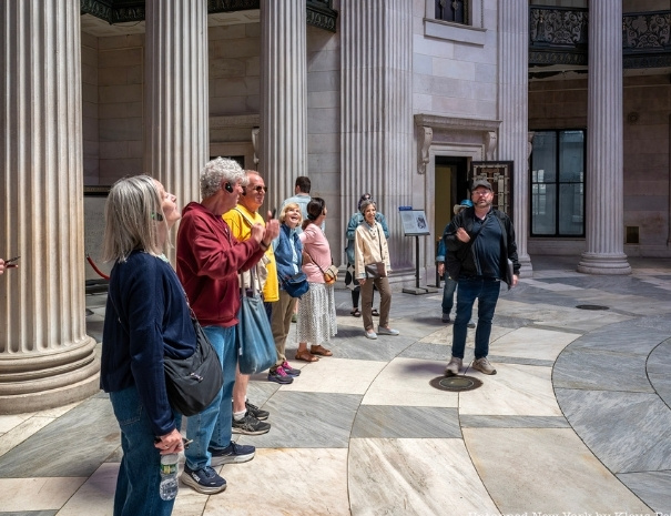 Untapped New York tour guests gazing upward at the soaring marble columns inside Federal Hall National Memorial in lower Manhattan