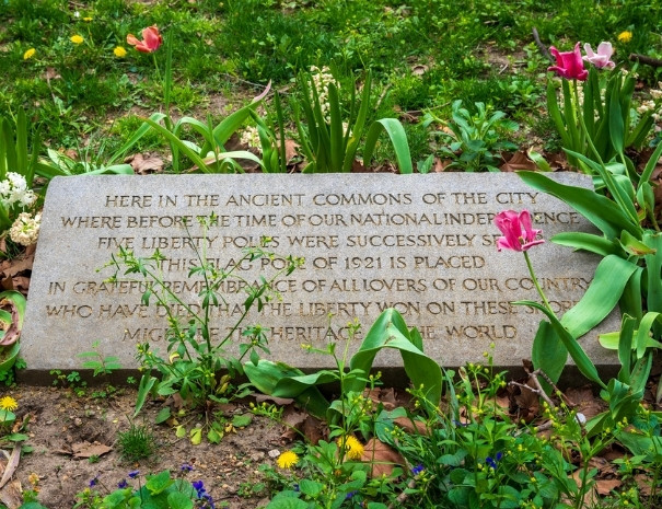Stone memorial marker surrounded by spring tulips in City Hall Park, Manhattan, commemorating the five Liberty Poles erected on the site before American independence