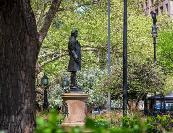 Bronze statue of Revolutionary-era Nathan Hale on a stone pedestal in a lower Manhattan park, surrounded by flowering spring trees