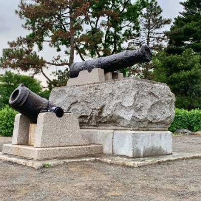 Two Revolutionary War-era cast iron cannons mounted on granite pedestals in Central Park, remnants of the 1776 battlefield.
