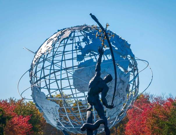 The Rocket Thrower sculpture silhouetted against the Unisphere in Flushing Meadows Corona Park, framed by red fall foliage