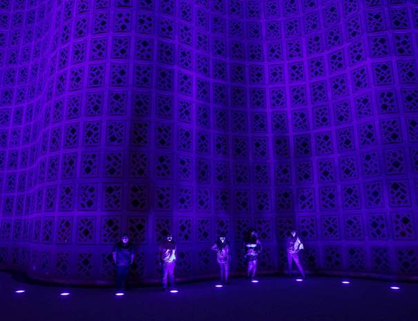 Visitors stand at the base of the New York Hall of Science Great Hall, its curving wall lit purple at night
