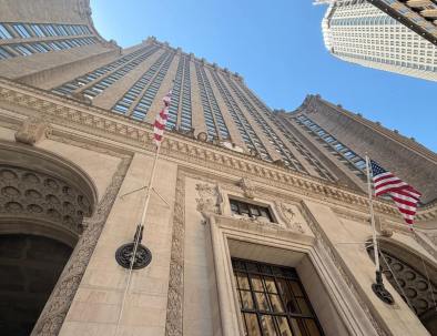 Looking up at the ornate limestone facade of the Helmsley Building on Park Avenue, with American flags flanking its central entrance and clock.